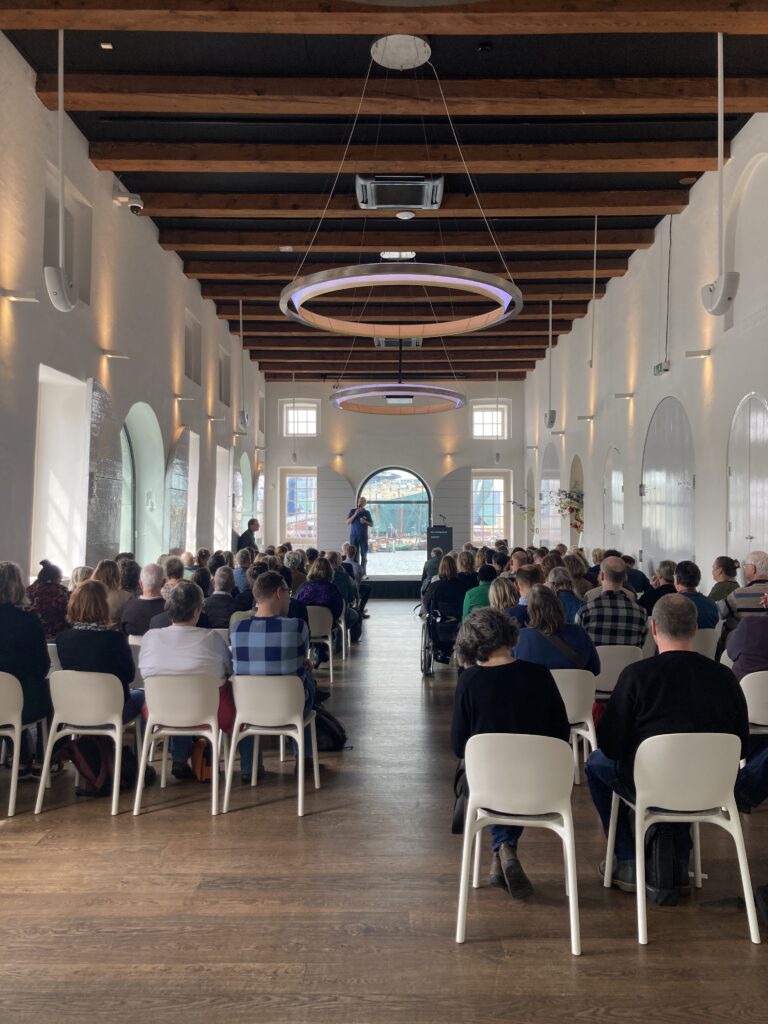 De grote zaal van het Scheepvaartmuseum, met ongeveer 100 mensen van achteren gezien.
